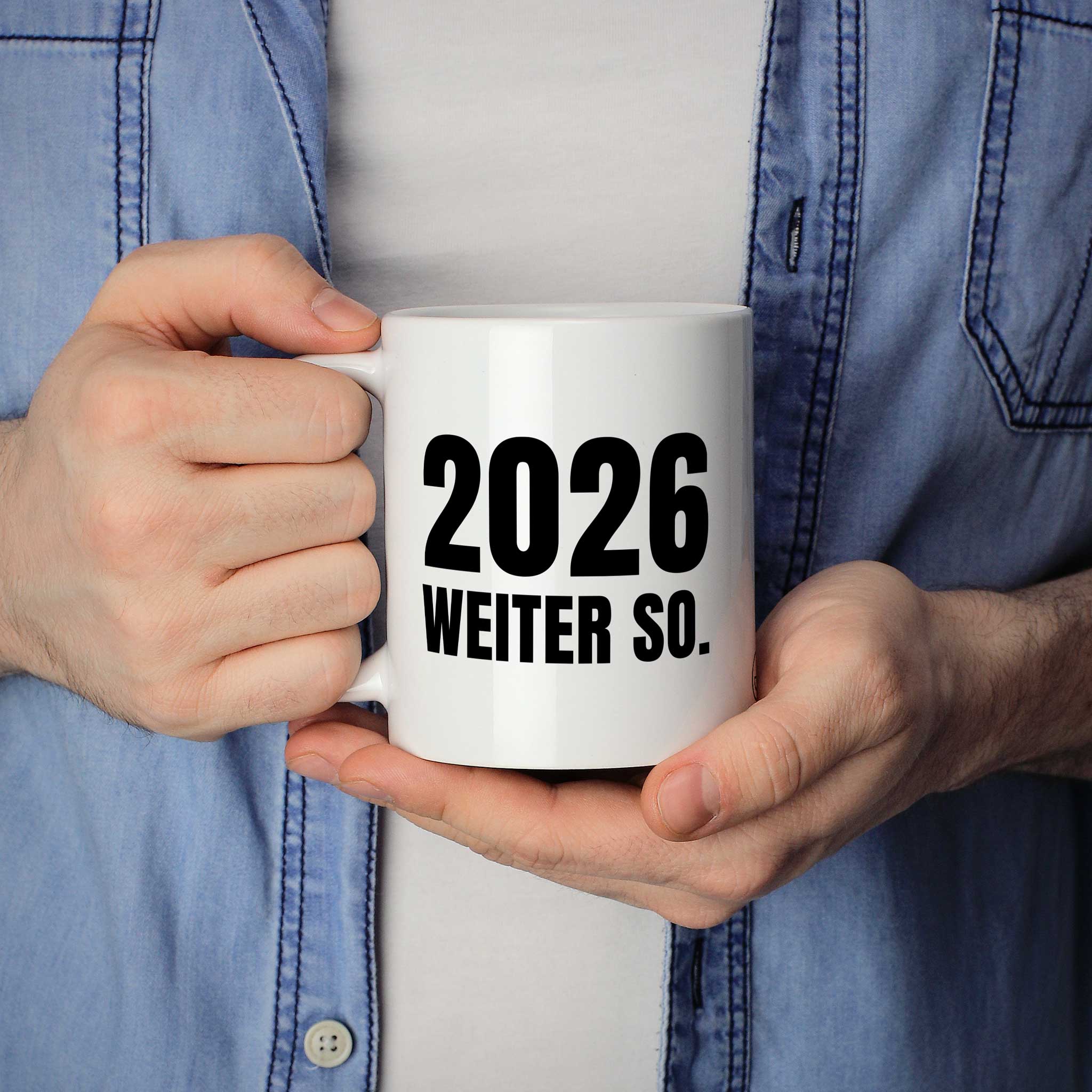 Brüllerware Statement-Tasse „2026. Weiter so.“ in der Hand gehalten – beidseitig bedruckte Kaffeetasse