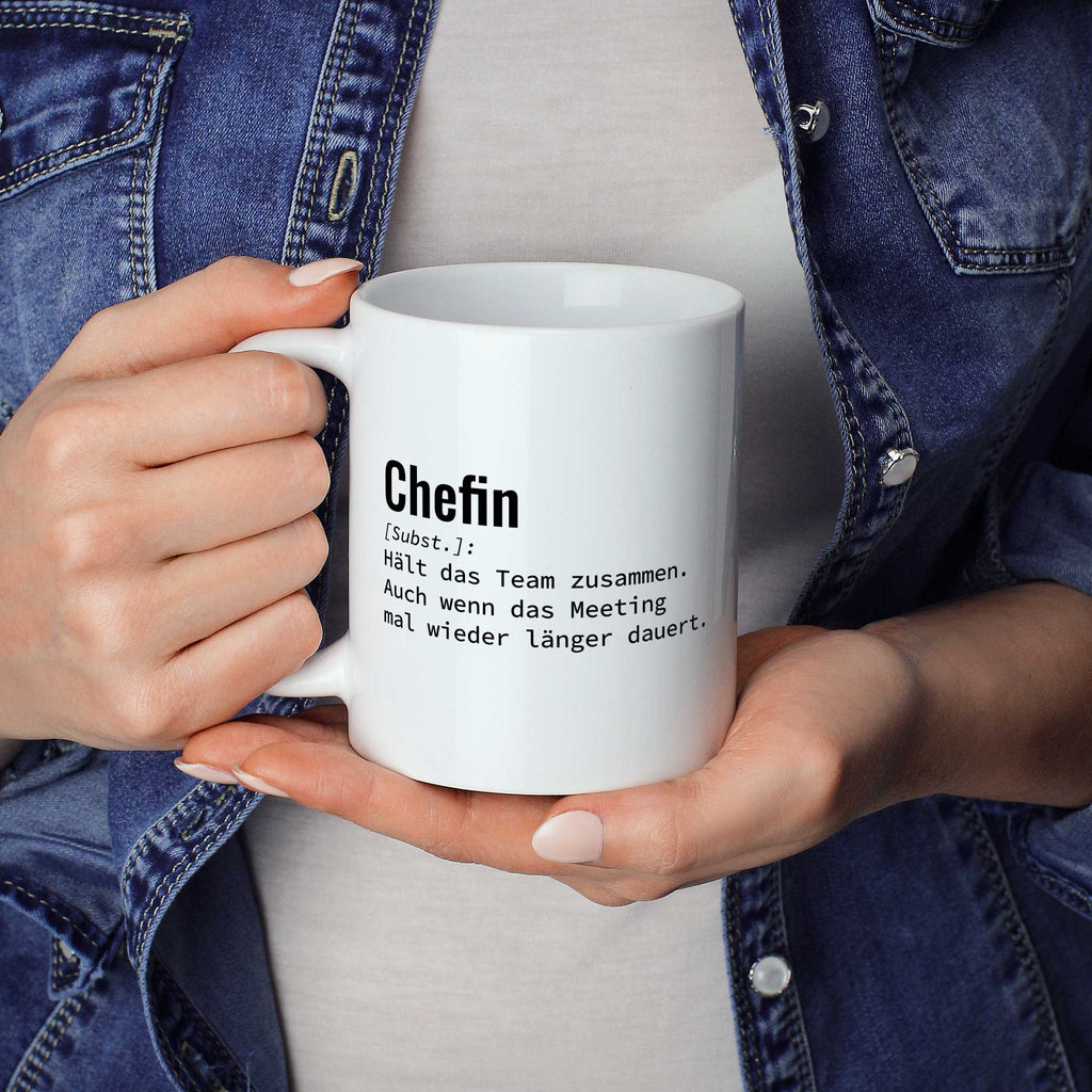 Person hält Tasse mit Spruch „Chefin [Subst.]: Hält das Team zusammen. Auch wenn das Meeting mal wieder länger dauert.“ in beiden Händen