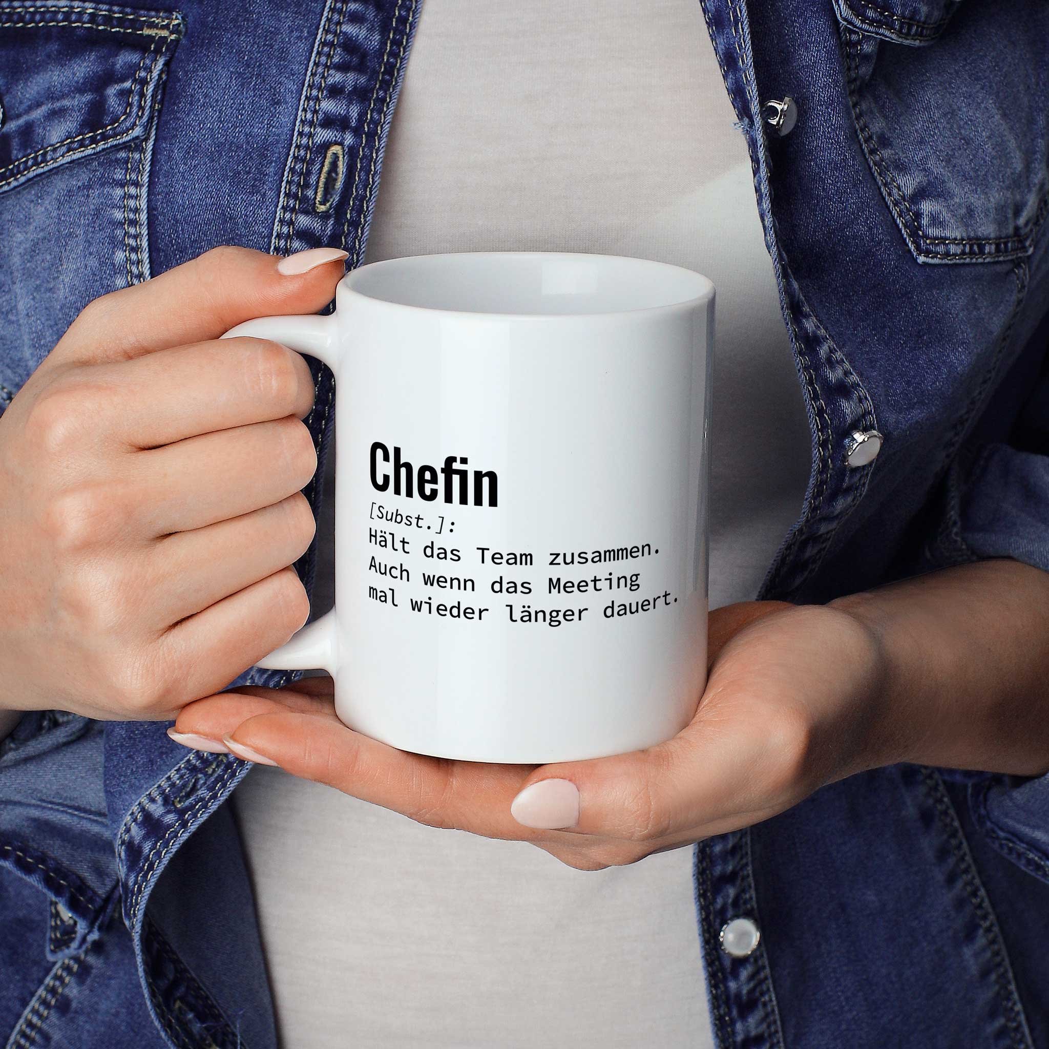 Person hält Tasse mit Spruch „Chefin [Subst.]: Hält das Team zusammen. Auch wenn das Meeting mal wieder länger dauert.“ in beiden Händen