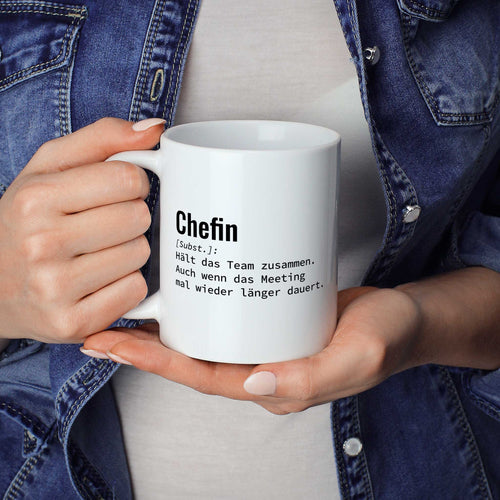 Person hält Tasse mit Spruch „Chefin [Subst.]: Hält das Team zusammen. Auch wenn das Meeting mal wieder länger dauert.“ in beiden Händen