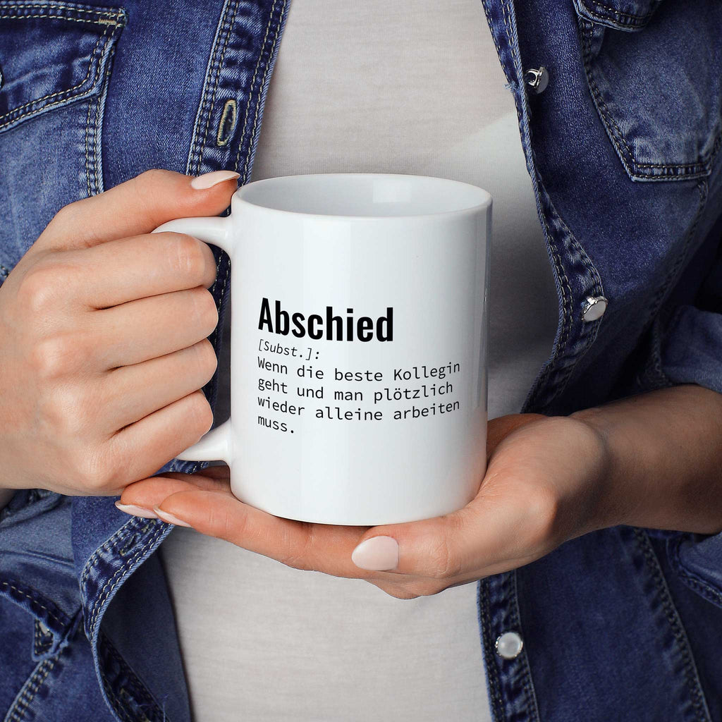 Person hält Tasse mit Spruch „Abschied [Subst.]: Wenn die beste Kollegin geht und man plötzlich wieder alleine arbeiten muss.“ in beiden Händen