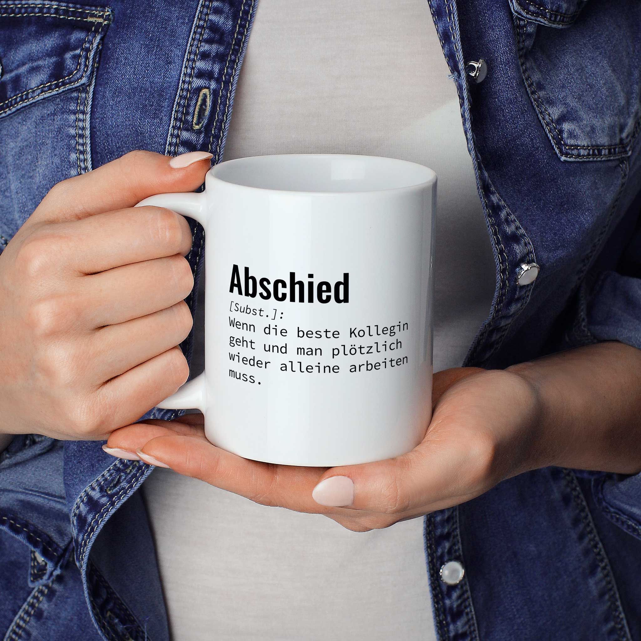 Person hält Tasse mit Spruch „Abschied [Subst.]: Wenn die beste Kollegin geht und man plötzlich wieder alleine arbeiten muss.“ in beiden Händen