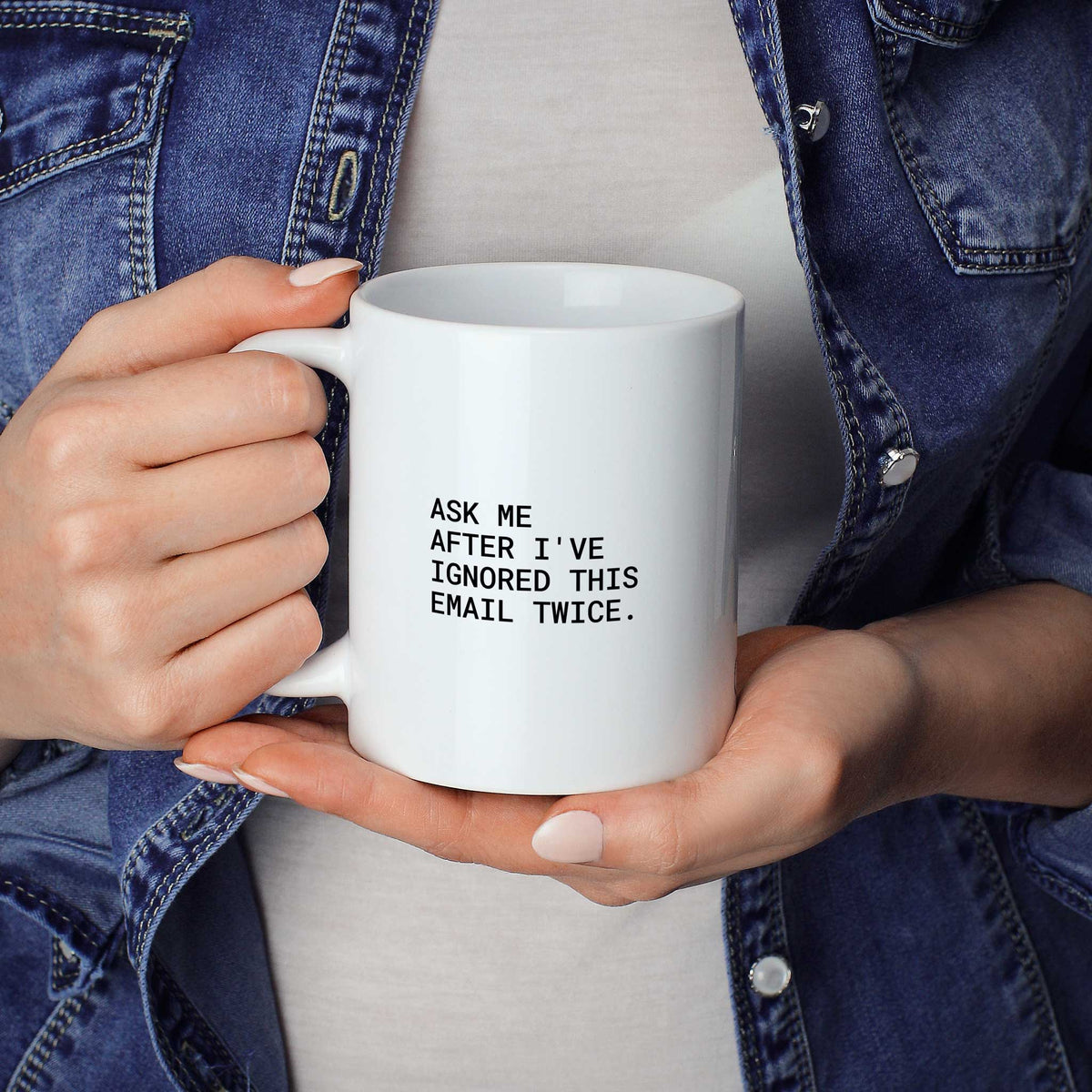 Person hält weiße Tasse mit dem Spruch „Ask me after I’ve ignored this email twice“ in beiden Händen