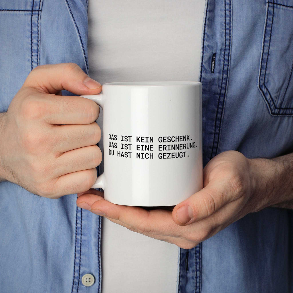 Brüllerware Statement-Tasse „Das ist kein Geschenk. Das ist eine Erinnerung: Du hast mich gezeugt.“ in der Hand gehalten – beidseitig bedruckte Kaffeetasse