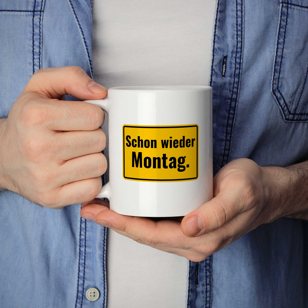 Brüllerware Statement-Tasse „Schon wieder Montag.“ in der Hand gehalten – beidseitig bedruckte Kaffeetasse