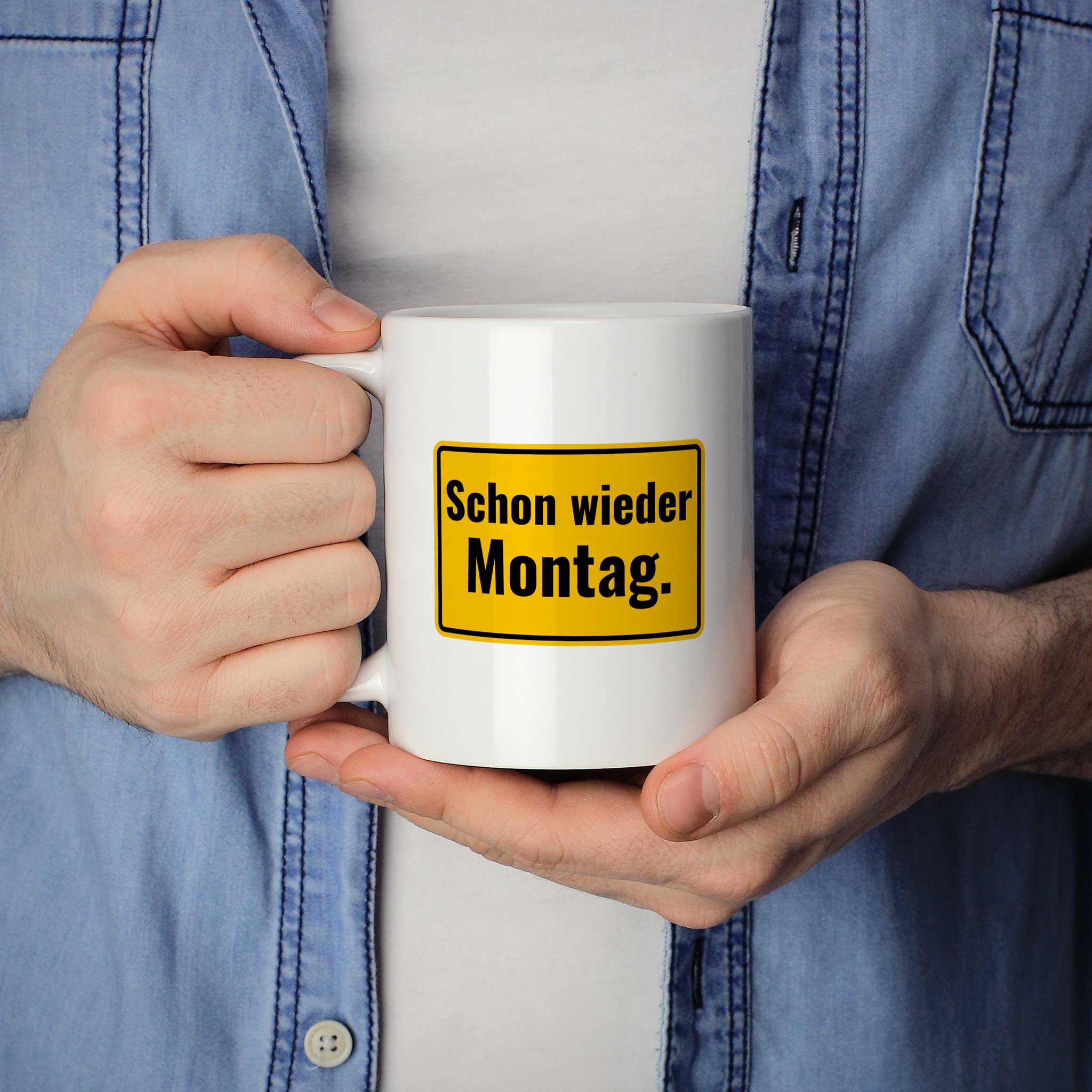 Brüllerware Statement-Tasse „Schon wieder Montag.“ in der Hand gehalten – beidseitig bedruckte Kaffeetasse