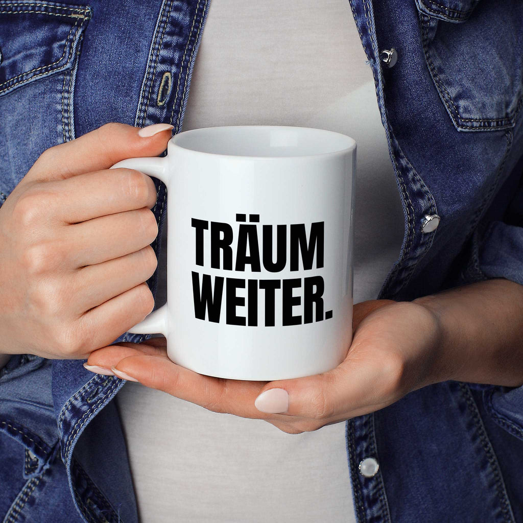 Brüllerware Statement-Tasse „Träum weiter.“ in der Hand gehalten – beidseitig bedruckte Kaffeetasse