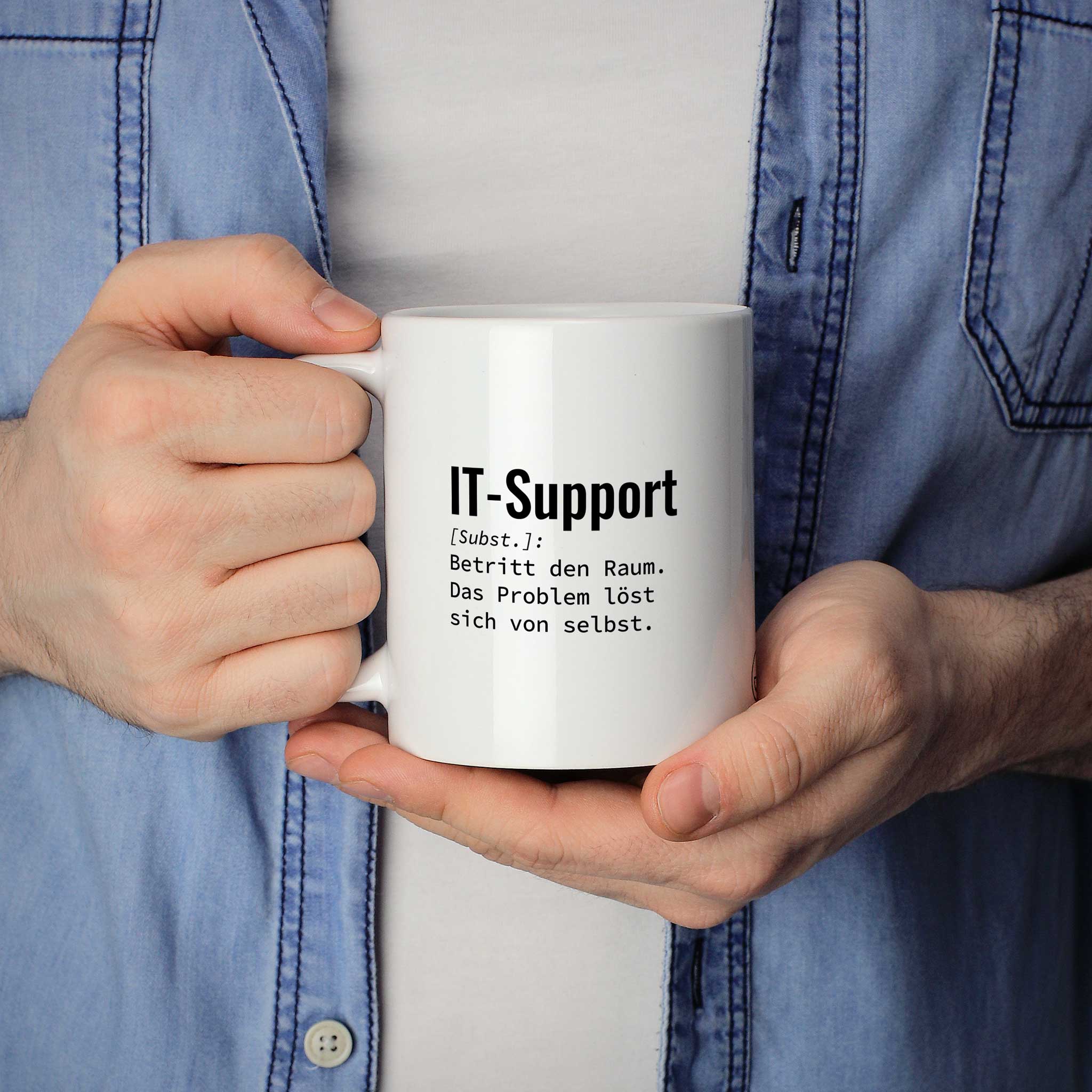 Person hält Tasse mit Spruch „IT-Support [Subst.]: Betritt den Raum. Das Problem löst sich von selbst.“ in beiden Händen