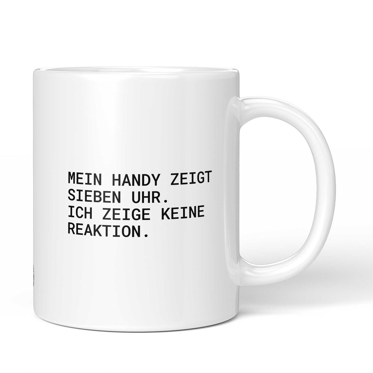Weiße Keramiktasse mit dem Spruch „Mein Handy zeigt sieben Uhr. Ich zeige keine Reaktion.“ von Brüllerware