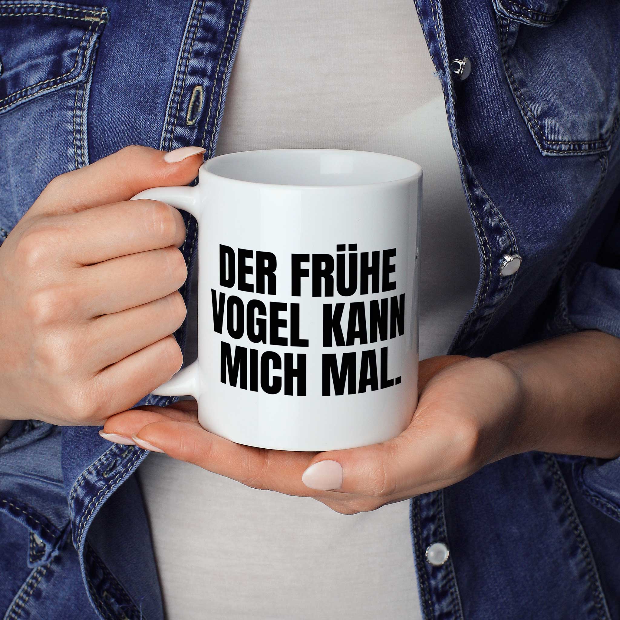 Frau hält lustige Tasse mit Spruch „Der frühe Vogel kann mich mal." – weiße Keramiktasse mit schwarzem Druck, Vorderansicht" in beiden Händen – Größenvergleich, 330 ml Keramiktasse