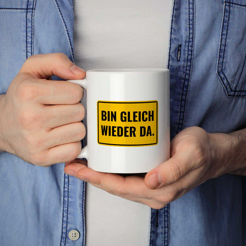 Mann hält lustige Tasse mit Spruch „Bin gleich wieder da." in beiden Händen – Größenvergleich, 330 ml Keramiktasse