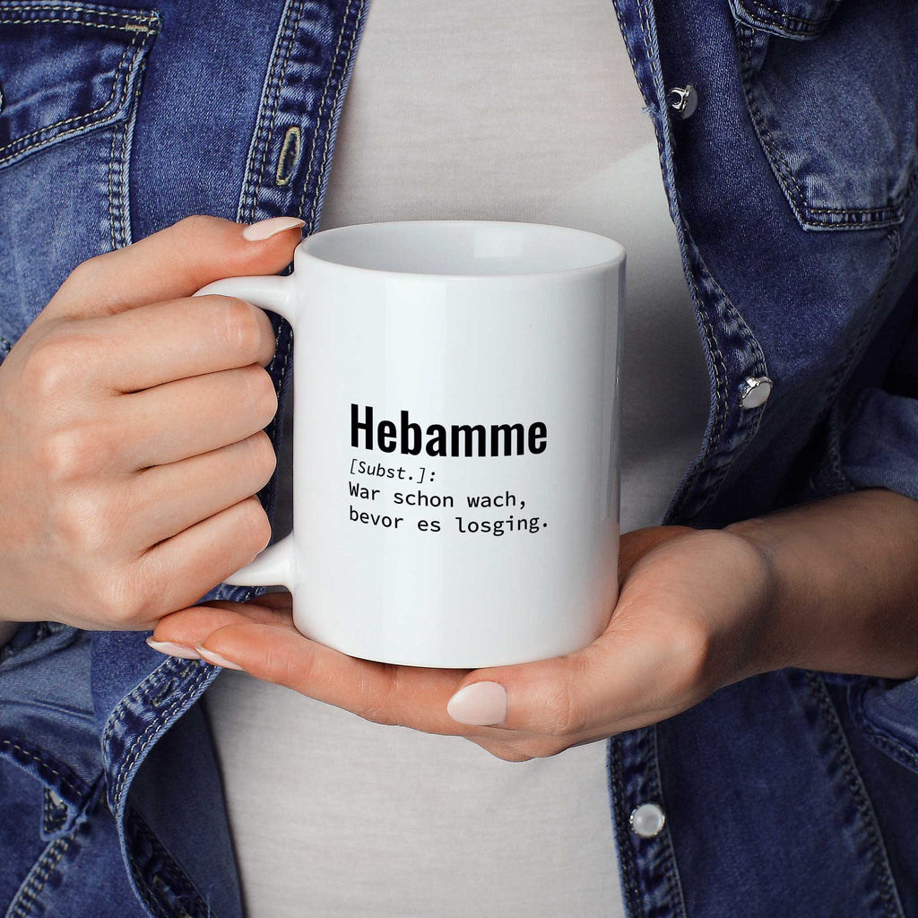 Frau hält lustige Tasse mit Spruch „Lustige Tasse mit Spruch „Hebamme: War schon wach, bevor es losging." – weiße Keramiktasse mit schwarzem Druck, Vorderansicht" in beiden Händen – Größenvergleich, 330 ml Keramiktasse
