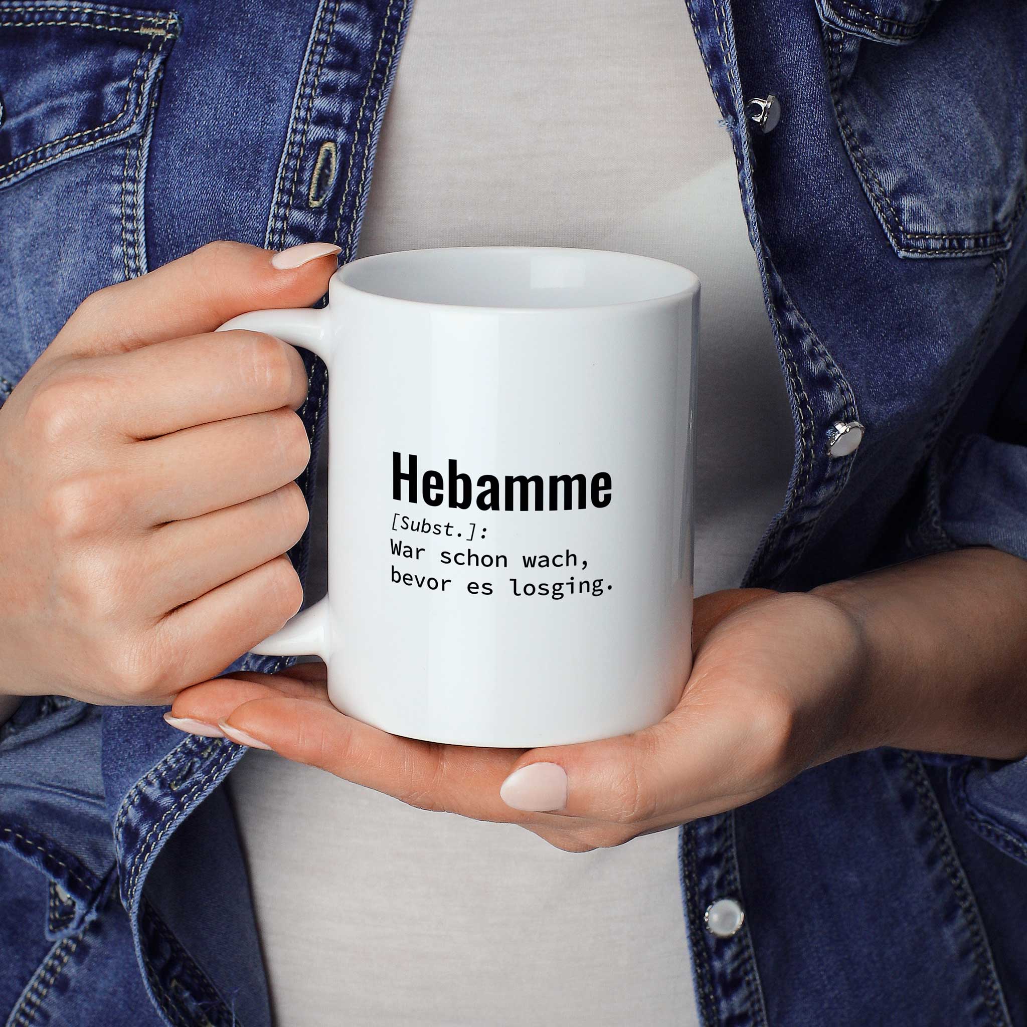 Frau hält lustige Tasse mit Spruch „Lustige Tasse mit Spruch „Hebamme: War schon wach, bevor es losging." – weiße Keramiktasse mit schwarzem Druck, Vorderansicht" in beiden Händen – Größenvergleich, 330 ml Keramiktasse