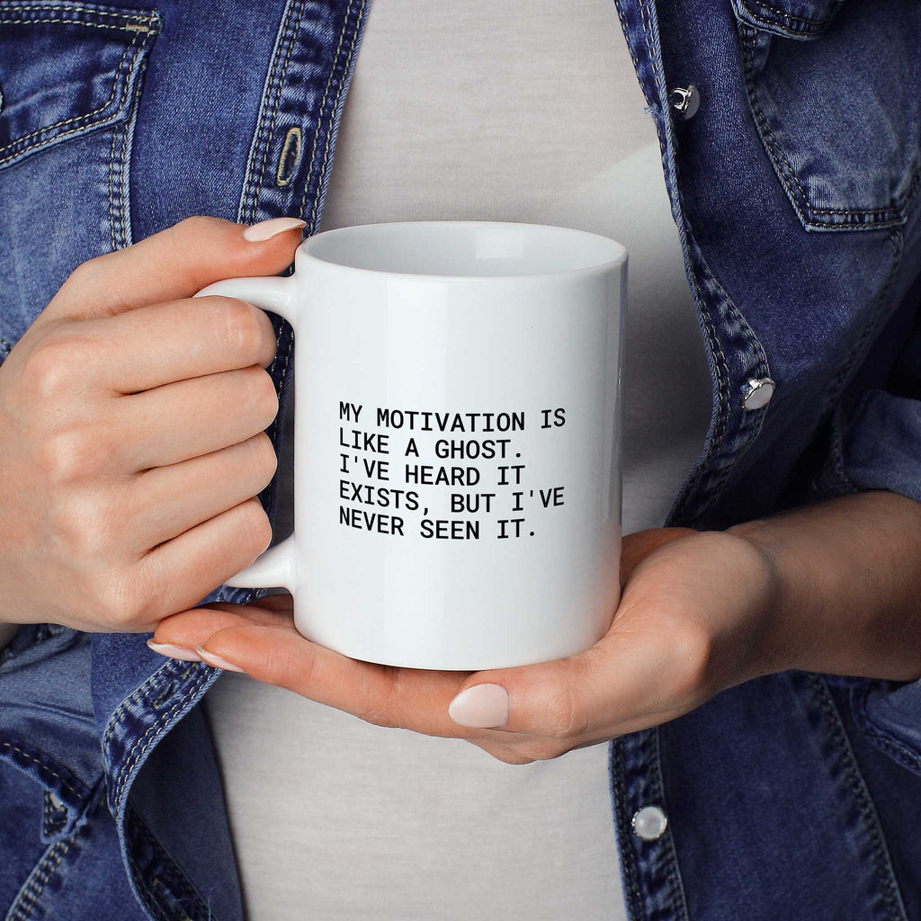 Person hält weiße Tasse mit dem Spruch „My motivation is like a ghost“ in beiden Händen