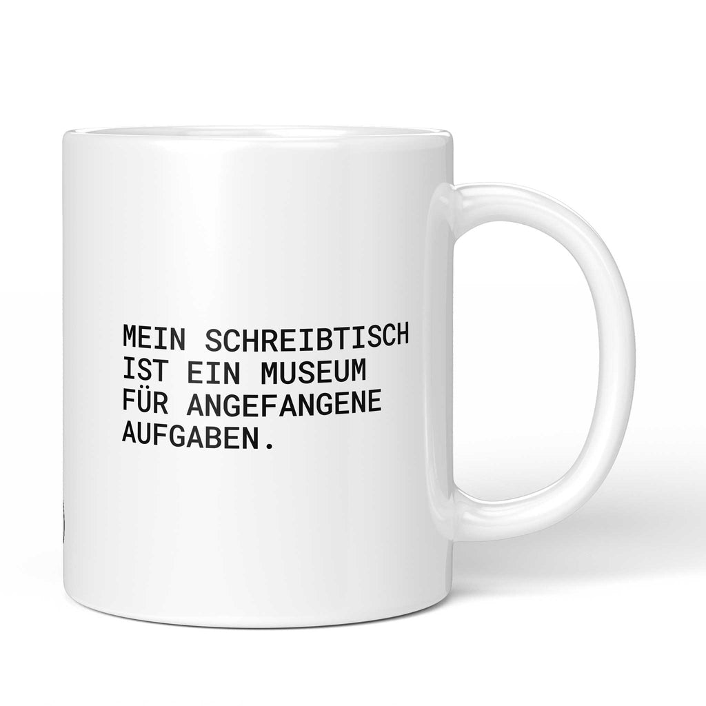Weiße Keramiktasse mit dem Spruch „Mein Schreibtisch ist ein Museum für angefangene Aufgaben.“ von Brüllerware