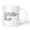 Weiße Tasse mit Spruch „Ich habe gerade 10 Minuten überlegt, ob ich aufstehen soll. Bin liegen geblieben.“ – Brüllerware