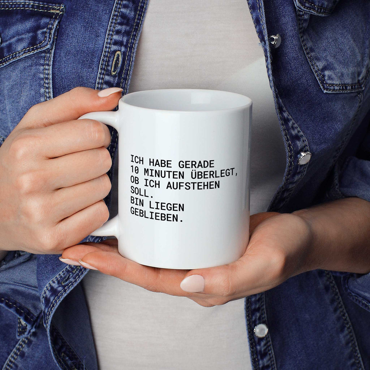 Weiße Tasse „Ich habe gerade 10 Minuten überlegt, ob ich aufstehen soll....“ in beiden Händen gehalten
