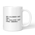 Weiße Tasse mit Spruch „Der Kalender sagt frei, die Realität sagt etwas anderes.“ – Brüllerware
