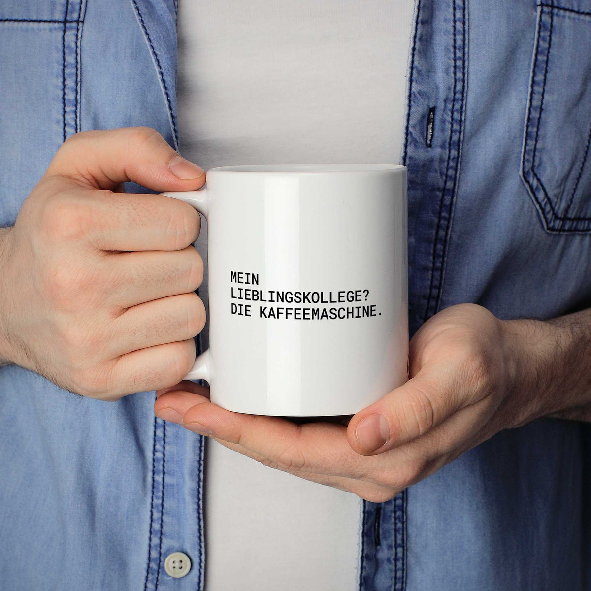 Weiße Tasse „Mein Lieblingskollege? Die Kaffeemaschine.“ in beiden Händen gehalten