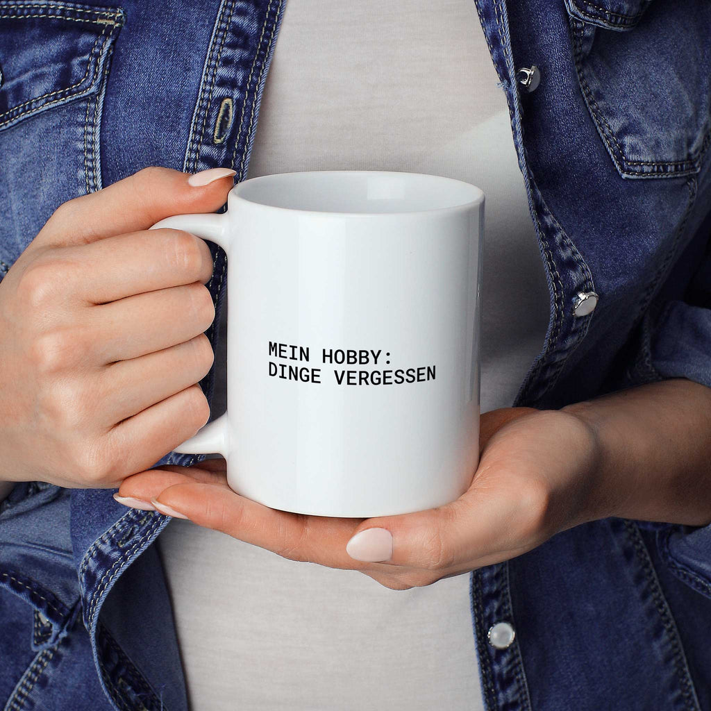 Brüllerware Statement-Tasse „Mein Hobby: Dinge vergessen“ in der Hand gehalten – beidseitig bedruckte Kaffeetasse