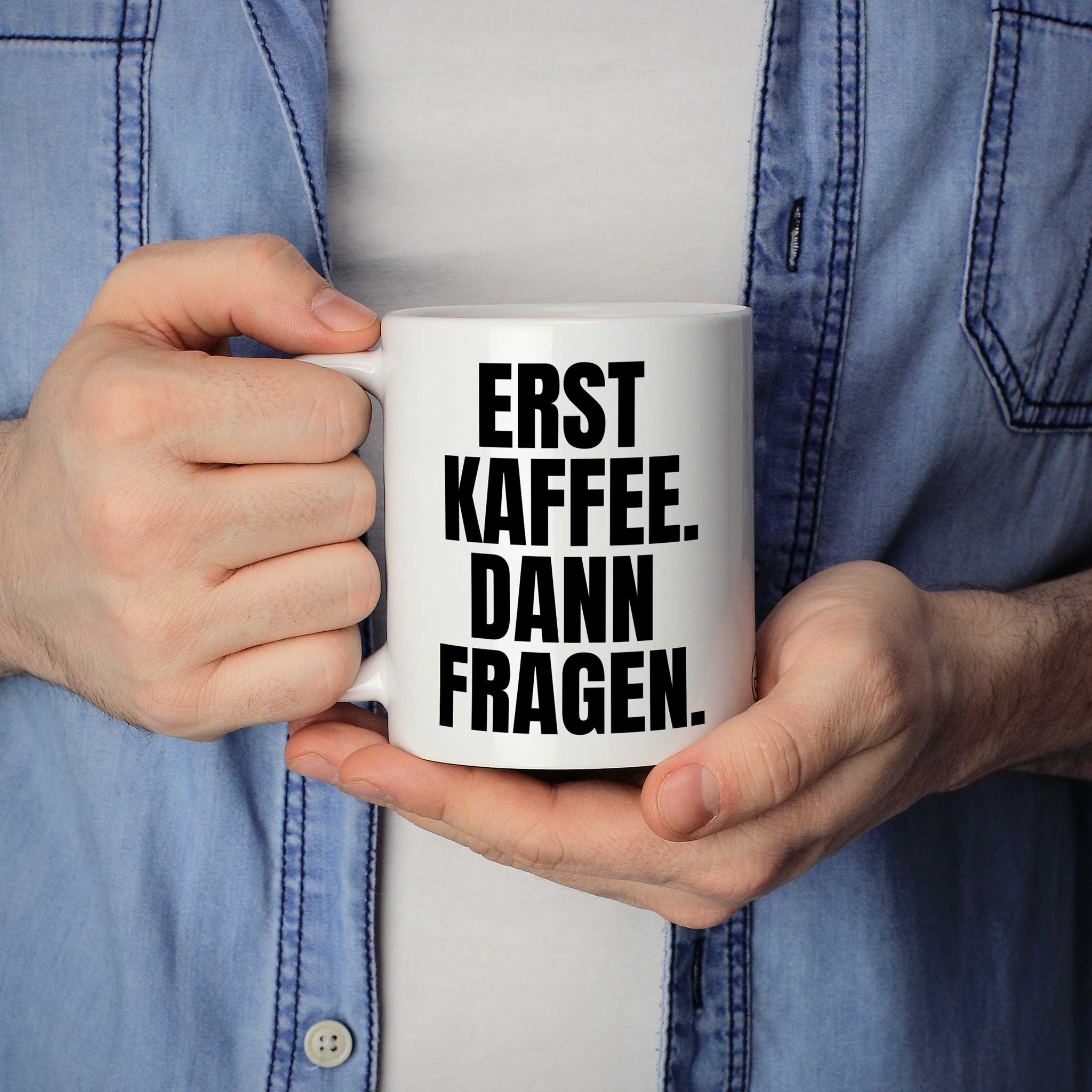 Person hält Tasse mit Spruch „Erst Kaffee. Dann Fragen.“ in beiden Händen