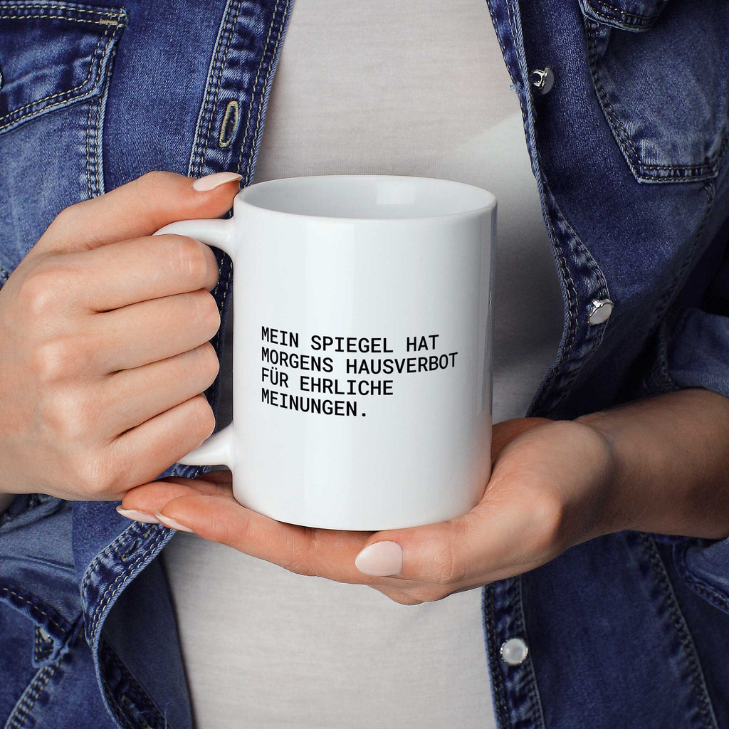Weiße Tasse „Mein Spiegel hat morgens Hausverbot für ehrliche Meinungen.“ in beiden Händen gehalten