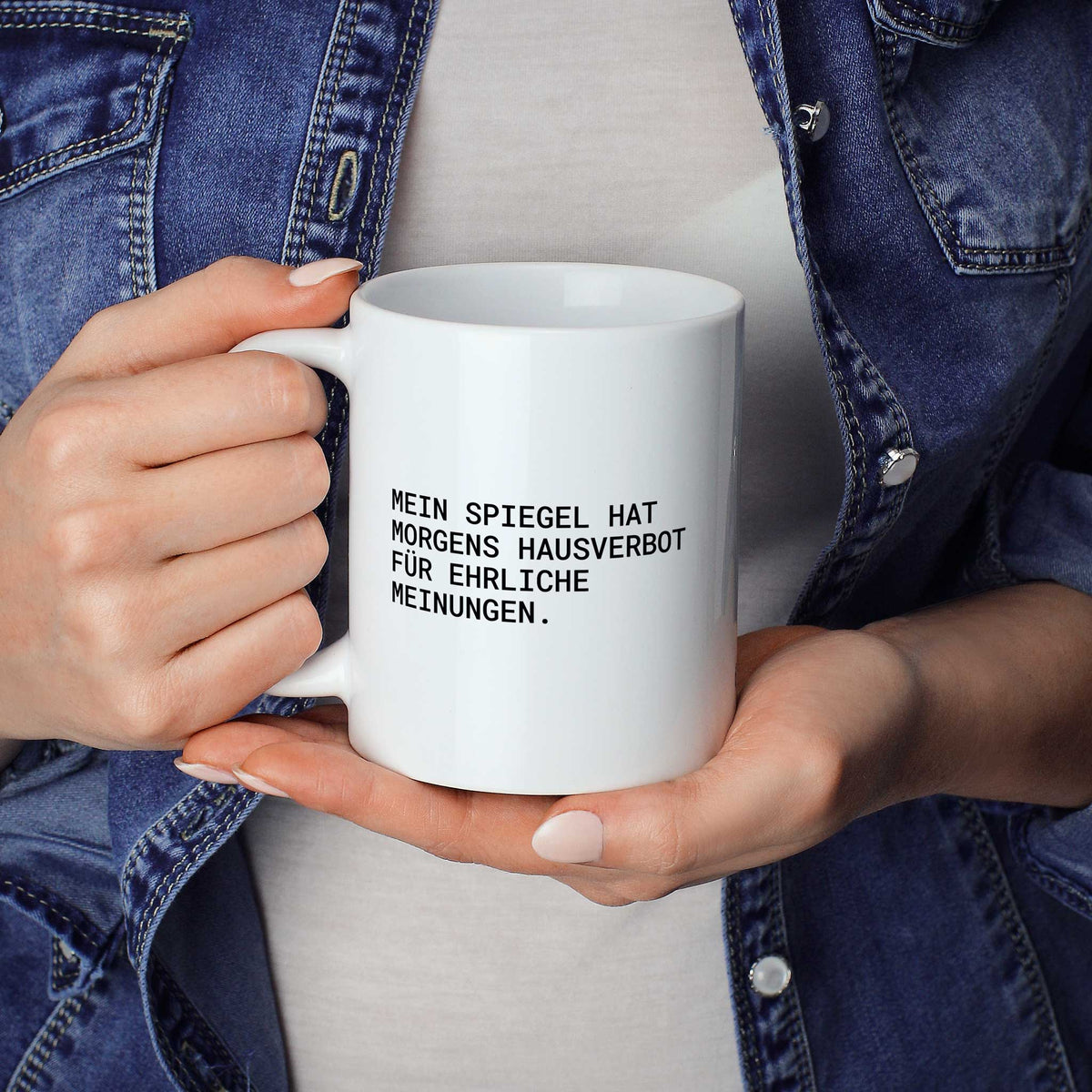 Weiße Tasse „Mein Spiegel hat morgens Hausverbot für ehrliche Meinungen.“ in beiden Händen gehalten