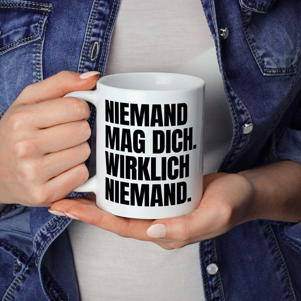 Brüllerware Statement-Tasse „Niemand mag dich. Wirklich niemand.“ in der Hand gehalten – beidseitig bedruckte Kaffeetasse