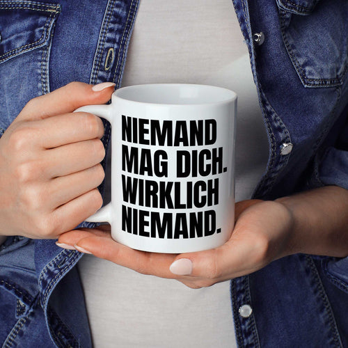 Brüllerware Statement-Tasse „Niemand mag dich. Wirklich niemand.“ in der Hand gehalten – beidseitig bedruckte Kaffeetasse