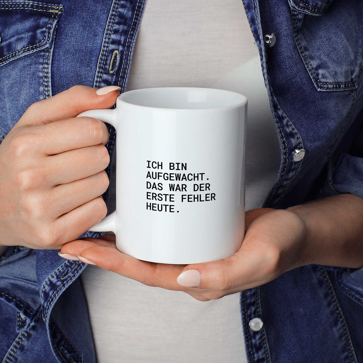 Weiße Tasse „Ich bin aufgewacht – das war der erste Fehler heute.“ in beiden Händen gehalten