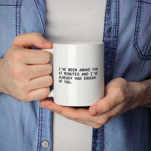 Weiße Tasse „I've been awake for 47 minutes and I've already had enough of...“ in beiden Händen gehalten