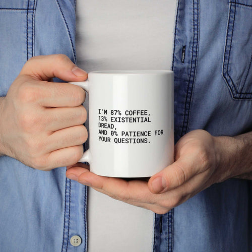 Weiße Tasse „I'm 87% coffee, 13% existential dread, and 0% patience for...“ in beiden Händen gehalten