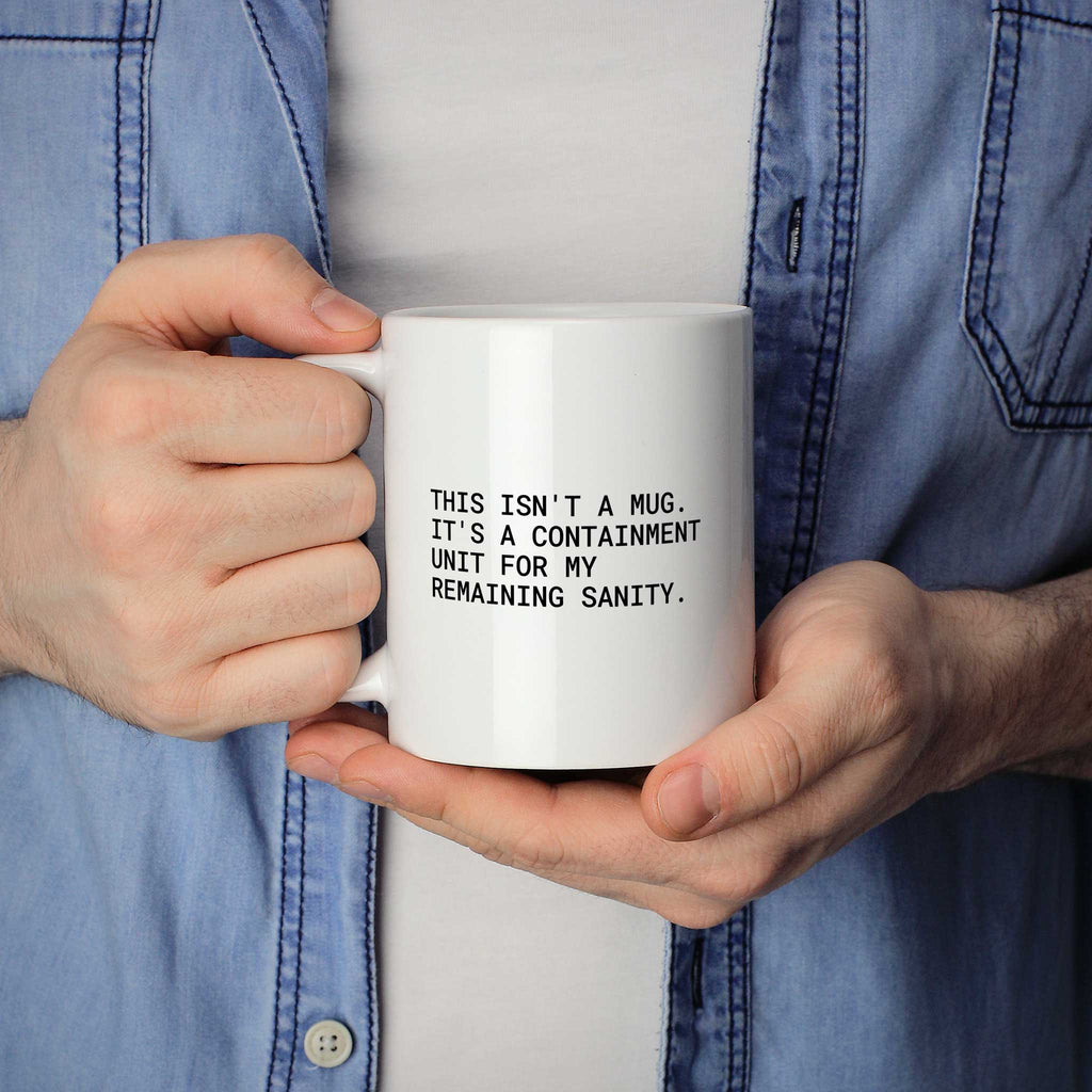 Weiße Tasse „This isn't a mug – it's a containment unit for my remaining...“ in beiden Händen gehalten