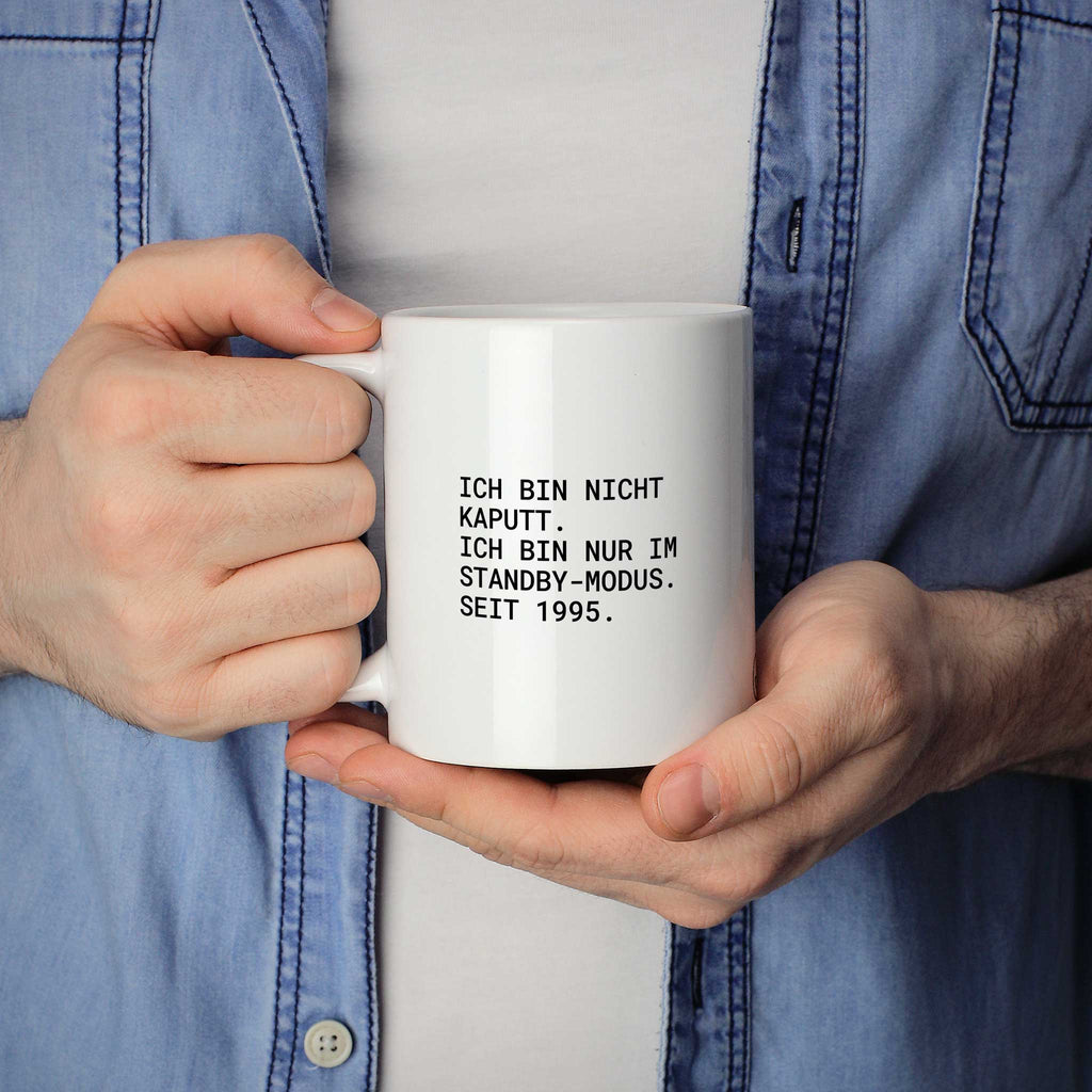 Weiße Tasse „Ich bin nicht kaputt – ich bin nur im Standby-Modus. Seit 1995.“ in beiden Händen gehalten