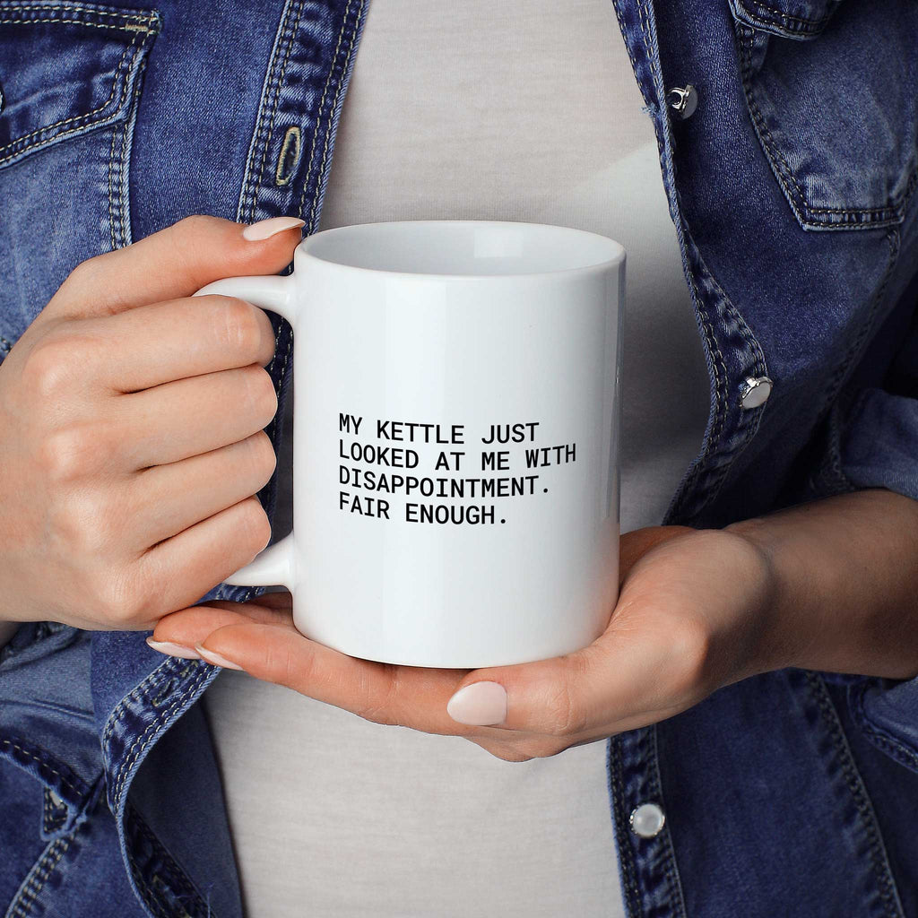 Weiße Tasse „My kettle just looked at me with disappointment. Fair enough.“ in beiden Händen gehalten