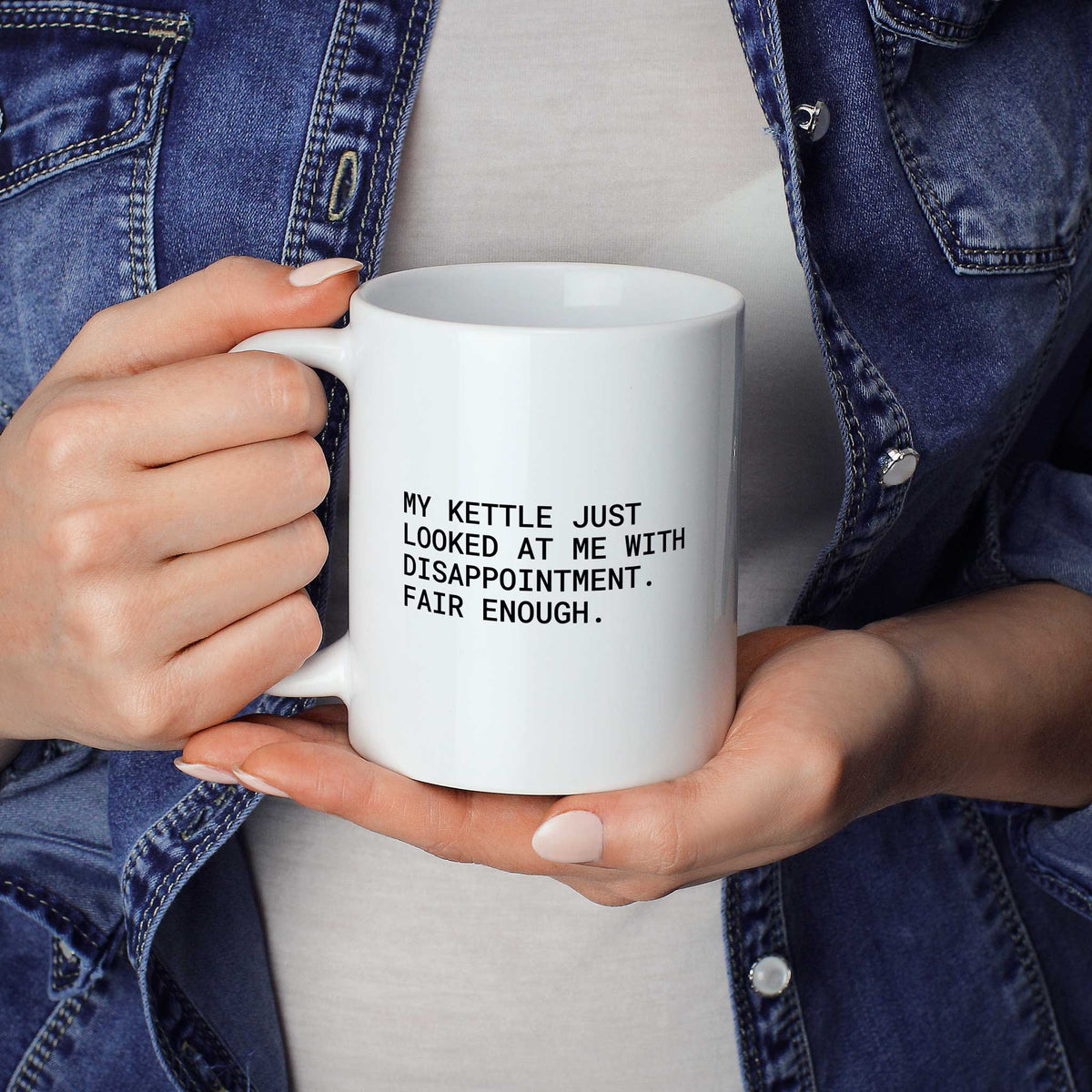 Weiße Tasse „My kettle just looked at me with disappointment. Fair enough.“ in beiden Händen gehalten