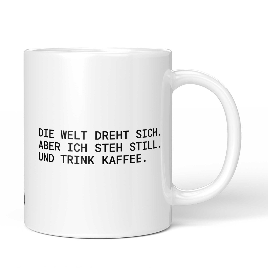 Weiße Tasse mit Spruch „Die Welt dreht sich – aber ich steh still. Und trink Kaffee.“ – Brüllerware