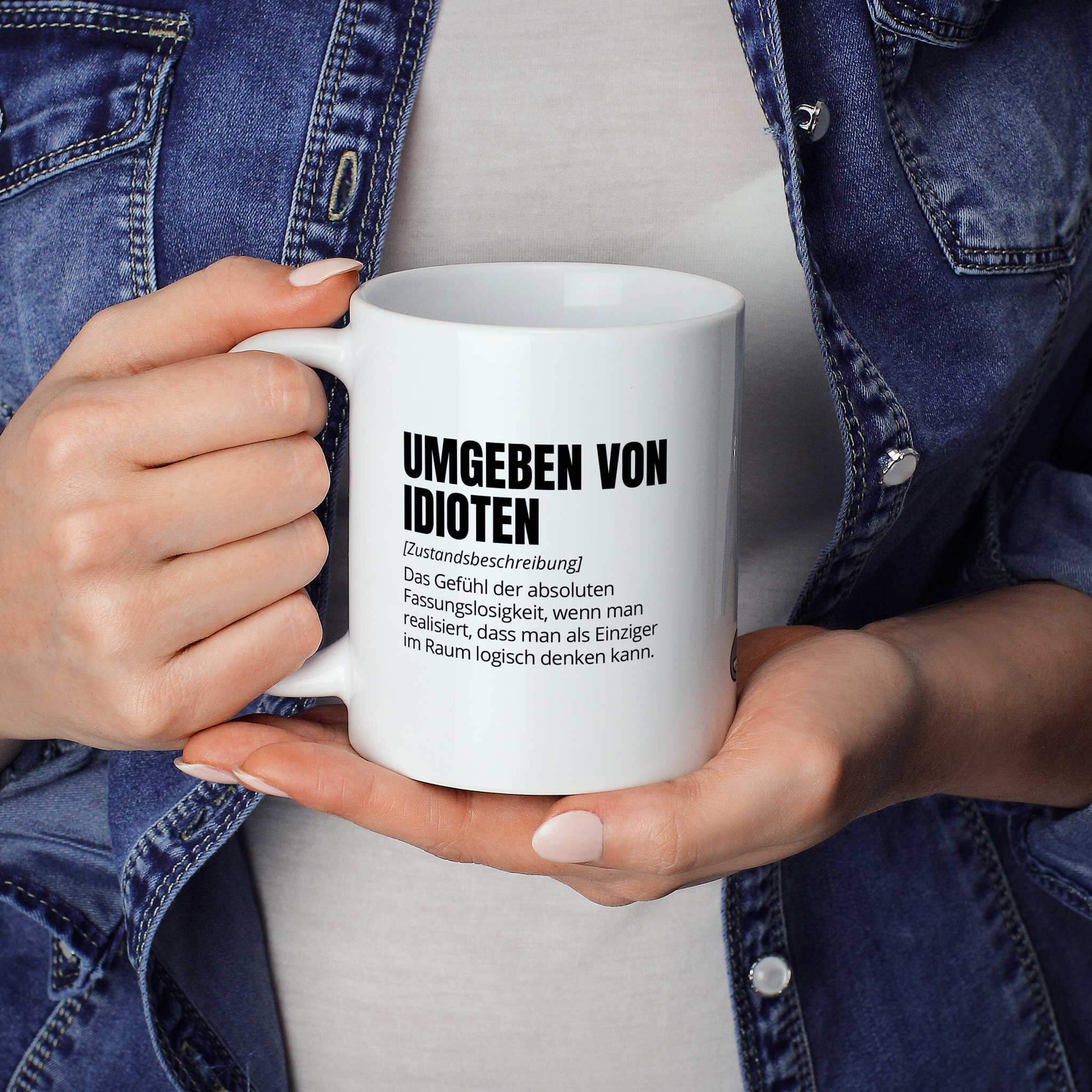 Lustige Tasse "Umgeben von Idioten" als Geschenkidee - Brüllerware Statement Becher in der Hand