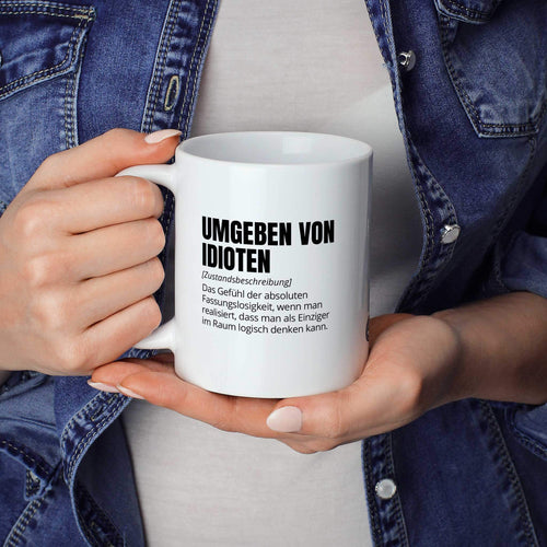Lustige Tasse "Umgeben von Idioten" als Geschenkidee - Brüllerware Statement Becher in der Hand