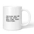 Weiße Keramiktasse mit dem Spruch „Zwischen mir und dem Tag steht noch eine Tasse. Mindestens.“ von Brüllerware